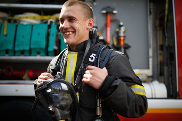 Photo of smiling firefighter standing near fire truck with fire hose