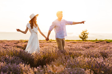 Photo of happy young man and woman dating, and walking together outdoor in lavender field - obrazy, fototapety, plakaty