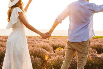 Image from back of caucasian couple man and woman holding hands, while walking outdoor in summer...