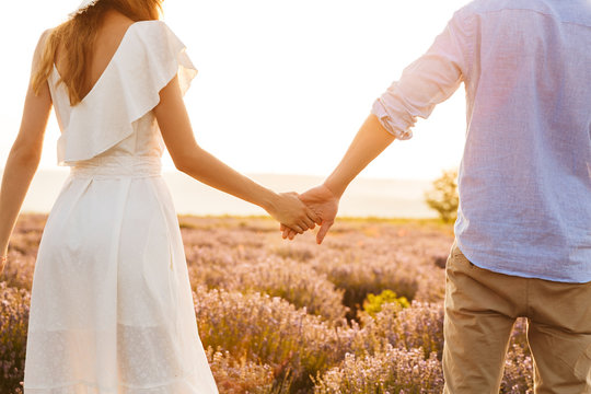 Cropped image from back of european couple man and woman holding hands, while walking outdoor in lavender field