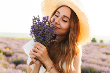 Cheerful young girl in straw hat smeling lavender bouquet
