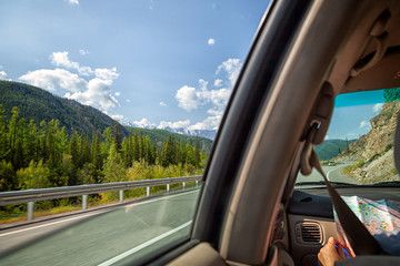 Woman inside the car driving and show map  on the country roadway between fields with brown grass and snowy mountains . Sun is shining. Shoot from the back