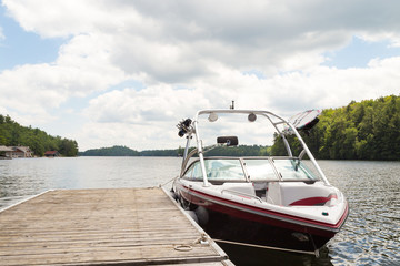 A wakeboard boat at a wooden dock in the Muskokas on a sunny day. - Powered by Adobe