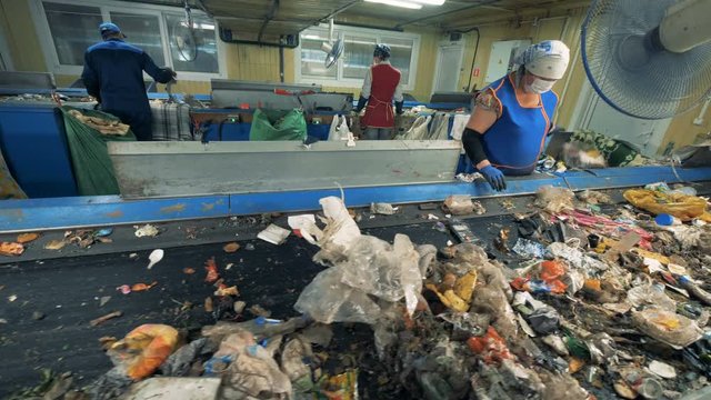 Garbage plant workers, close up. People sort trash on conveyors at a factory.