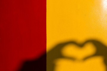 Silhouette of heart-shape hand on the bright yellow and red background.