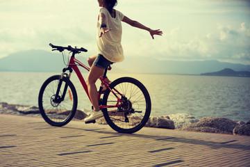handsfree woman riding a bike on sunny seaside with arms outstretched