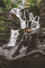 Fototapeta na wymiar man sitting at rock with waterfall on background
