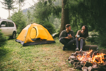 couple sitting near fire and drink hot tea. hiking concept. - obrazy, fototapety, plakaty