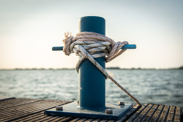 mooring bollard with a rope and a knot in front of water - obrazy, fototapety, plakaty