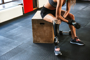 Portrait of young disabled invalid woman wearing prosthesis in tracksuit, training and lifting...