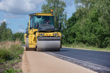 Yellow heavy vibration roller at asphalt pavement works. Road repairing in city. Road construction workers repairing highway road on sunny summer day. Heavy machinery, loaders and trucks