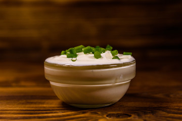 Glass bowl with sour cream and chopped green onion on wooden table