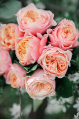 a bridal bouquet of pink, peach, orange austine english roses lies on flowering apricot branches, apple and almond trees