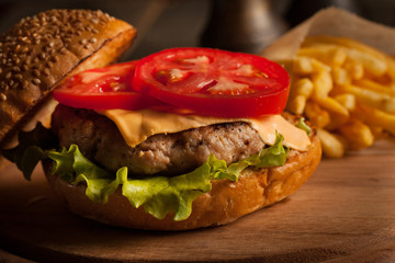 Home made hamburger with beef, onion, tomato, lettuce and cheese. Fresh burger close up on wooden rustic table with potato fries, beer and chips. Cheeseburger.