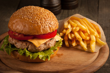 Home made hamburger with beef, onion, tomato, lettuce and cheese. Fresh burger close up on wooden rustic table with potato fries, beer and chips. Cheeseburger.