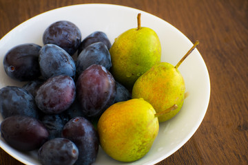 Pears and plums on a white plate. Ripe pear and plums lie on a white plate. Summer food with fresh fruits in a plate.
