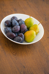 Pears and plums on a white plate. Ripe pear and plums lie on a white plate. Summer food with fresh fruits in a plate.