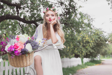 beautiful young bride riding bicycle with flower basket and looking at camera