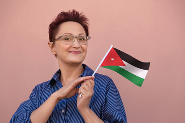 Jordan flag. Woman holding Jordan flag. Nice portrait of middle aged lady 40 50 years old with a national flag over pink wall background outdoors.