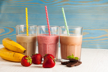 Long glasses of milkshakes with chocolate, strawberry, banana, with ice cream on white and blue...