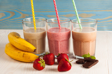 Long glasses of milkshakes with chocolate, strawberry, banana, with ice cream on white and blue...