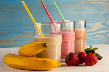 Long glasses of milkshakes with chocolate, strawberry, banana, with ice cream on white and blue...