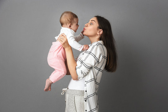 Image of happy young woman mother holding in hands her little child, isolated over gray background