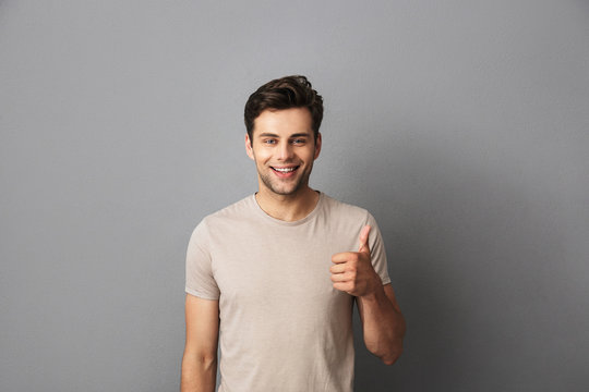 Image of attractive man 30s having stubble showing thumb up with happy smile, isolated over gray background