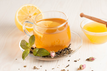 Closeup of cup of tea with tea leaves, mint on vintage wooden background. Black herbal tea with lemon, ginger and honey. hot winter drink