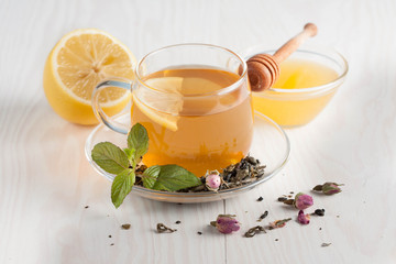 Closeup of cup of tea with tea leaves, mint on vintage wooden background. Black herbal tea with lemon, ginger and honey. hot winter drink