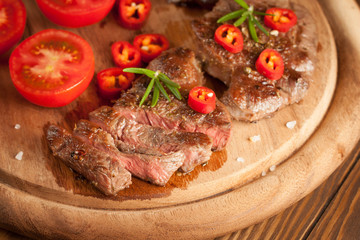 grilled fillet steak with tomatoes and roast vegetables on an old wooden board, background.