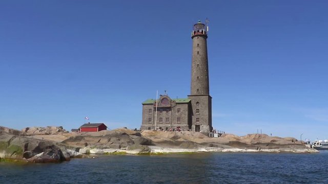 Slow motion pov view from a boat of a tall lighthouse, on a rocky island bengtskar, on a sunny summer day, in saaristomeri national park of the finnish archipelago, in Varsinais-suomi, Finland