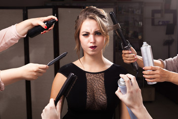 beautiful wriggling model is surrounded by many hands holding hair curler, sprays and brushes.....