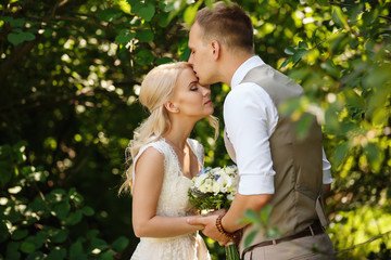 Naklejka premium Wedding day. Gentle photo of young newlyweds, kissing each other, closing their eyes and enjoying time spending together after wedding ceremony in the park.