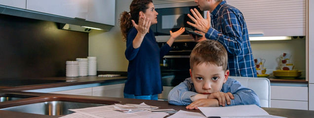 Sad boy looking at camera while his parents argue in the kitchen