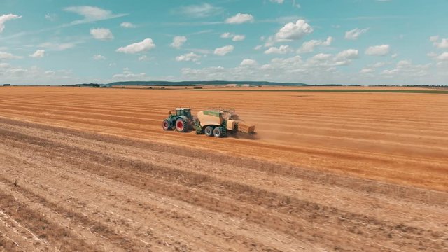 Aerial view flying over wheat field and combine harvester tractor with trailer that makes stacks of wheat at summers day 4K.
