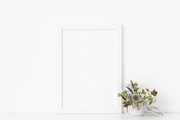 Modern white a4 portrait frame mockup with small bouquet of dried flowers in pot on white wall background. Empty frame, poster mock up for presentation design. 