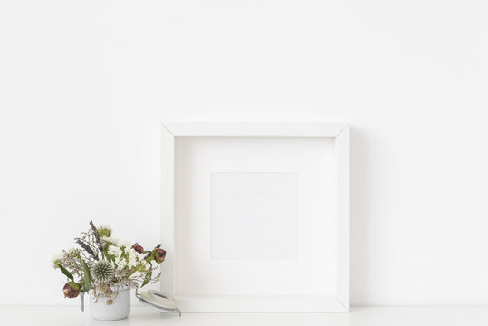 Stylish white square portrait frame mockup with small bouquet of dried flowers in small white pot on white wall background. Empty frame, poster mock up for presentation design. 