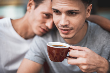Smiling male hugging optimistic comrade. He tasting appetizing cup of coffee during conversation