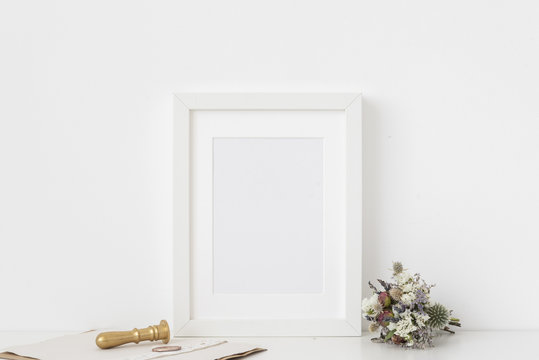 Cute white a5 portrait frame mockup with bouquet of dried flowers, gold stamp and printing on white wall background. Empty frame, poster mock up for presentation design. 