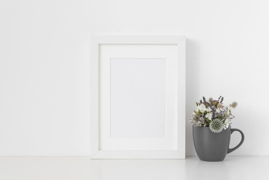 White A5 portrait frame mockup with small bouquet of dried flowers in gray mug on white wall background. Empty frame, poster mock up for presentation design.