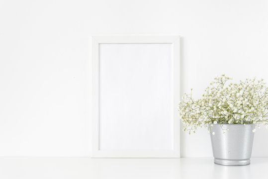Cute white frame mockup A4 in interior. Frame mock up background for poster or photo frame for bloggers, social media, lettering, art and design. Indoor, frame on table with flowers in metal bucket 