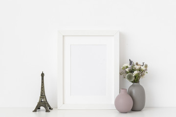 White a5 portrait frame mockup with dried field wild flowers, vases and Eiffel Tower on and white wall background. Empty frame, poster mock up for presentation design. 
