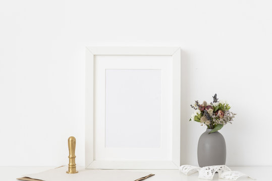 White a5 portrait frame mockup with dried field wild flowers in vase and gold stamp on white wall background.  Template frame for text, lettering, modern art.
