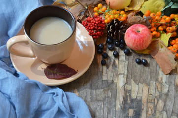 Flat lay of composed cup with black coffee on wood table with ripe berries of rowan and dark foliage. Cappuccino or latte or tea on a vintage table. fallen leaves, ripe apples, berries. Copy space