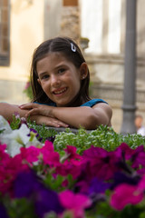 Cute little girl portrait by colorful flowers. Smiling kid poses by garden outdoors. Child innocence, happiness concepts