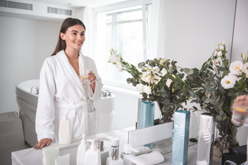 Portrait of beaming girl drinking cup of delicious beverage. She looking at mirror while standing...