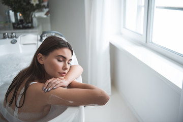 Portrait of calm girl sleeping while taking bath during sunny day opposite window in room