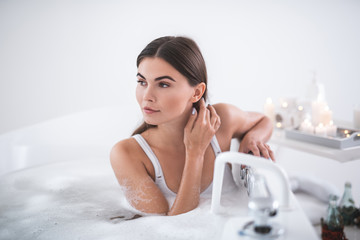 Portrait of orderly woman touching hair with hand while resting in cozy bath in apartment