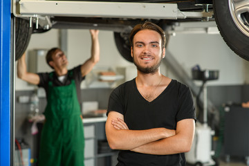 A young handsome guy in a black T-shirt is photographed against the background of a working mechanic
